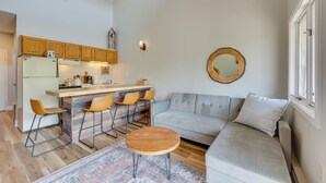Un espacio habitable pequeño con kitchenette, un sofá, una mesa redonda de madera y un tapete estampado.