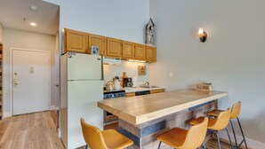 Una cocina con armarios de madera, una isla central con taburetes de bar, un refrigerador y una lámpara fijada a la pared.