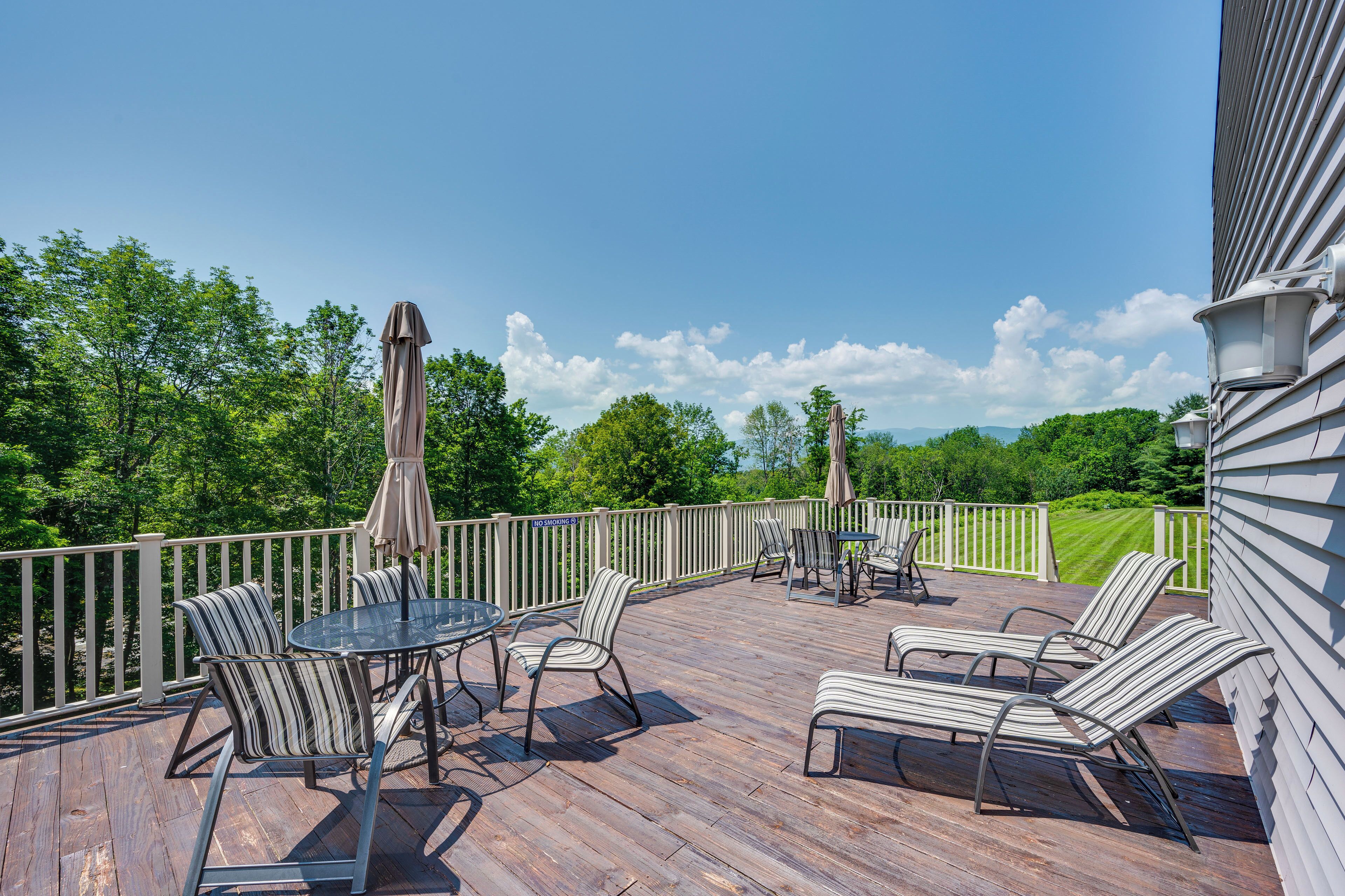 A wooden deck with outdoor furniture, including chairs and a table, and a view of a green landscape.