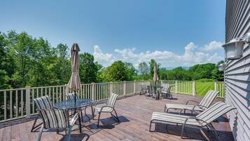 A wooden deck with outdoor furniture, including chairs and a table, and a view of a green landscape.