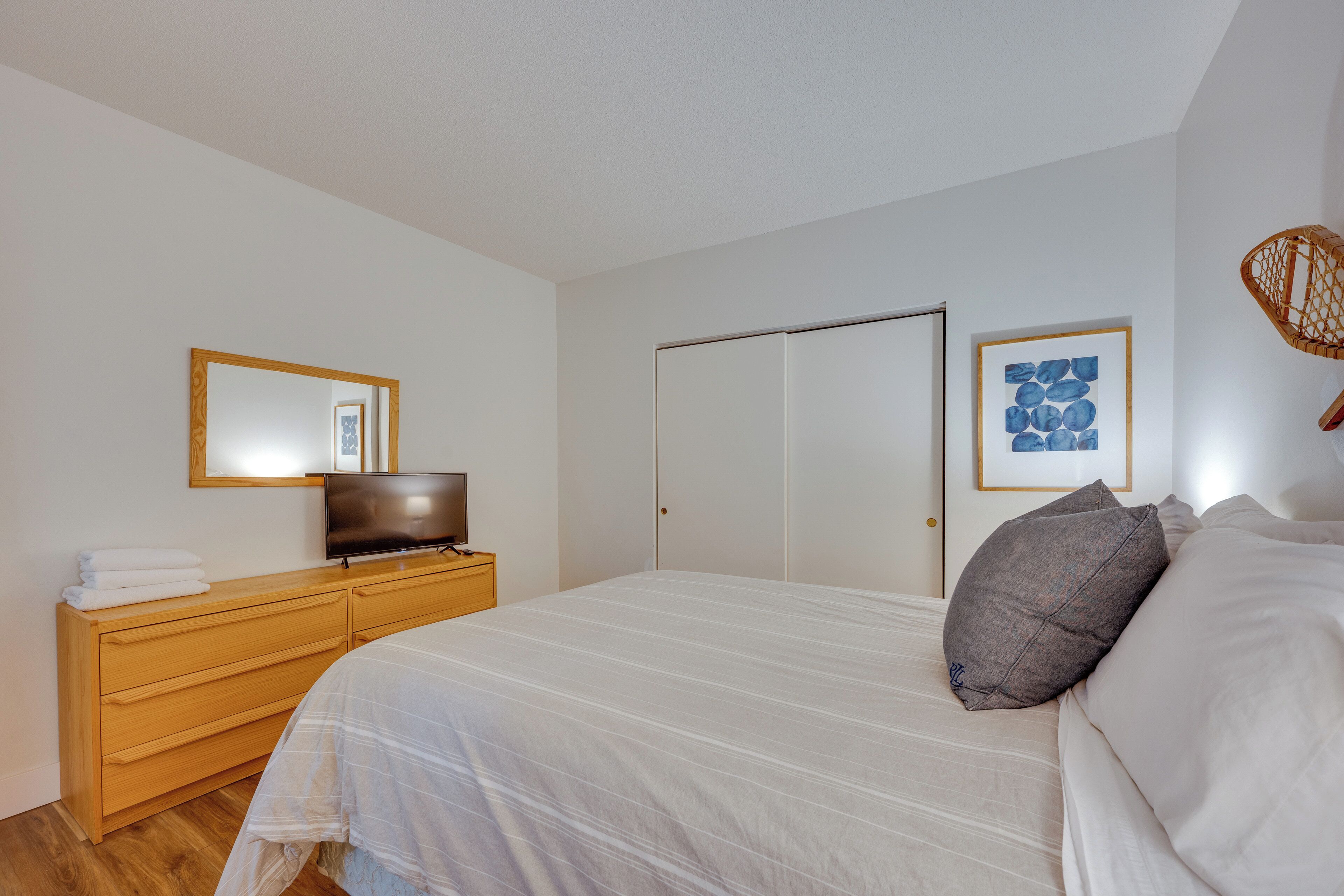 A bedroom with a bed, a TV on a dresser, a wardrobe, and a framed picture on the wall.