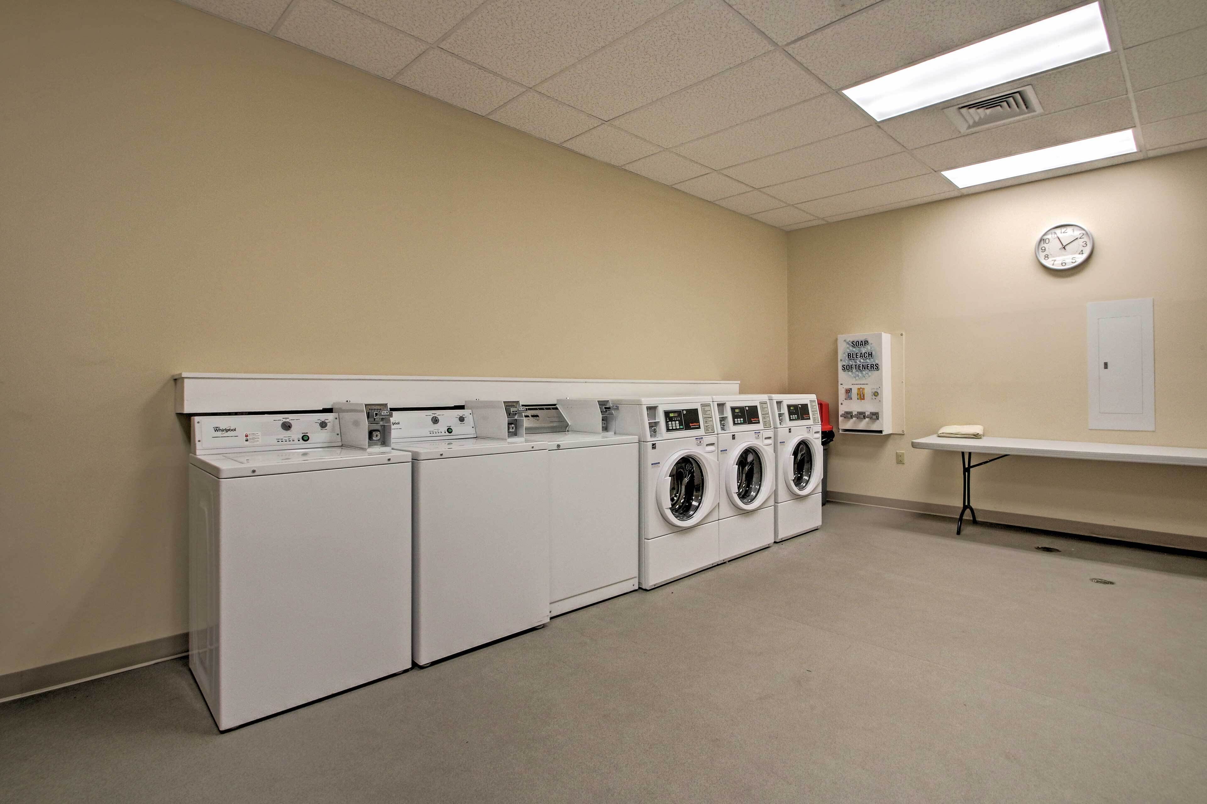 A laundry facility with multiple washing machines and dryers, a clock on the wall, and a table with a towel.