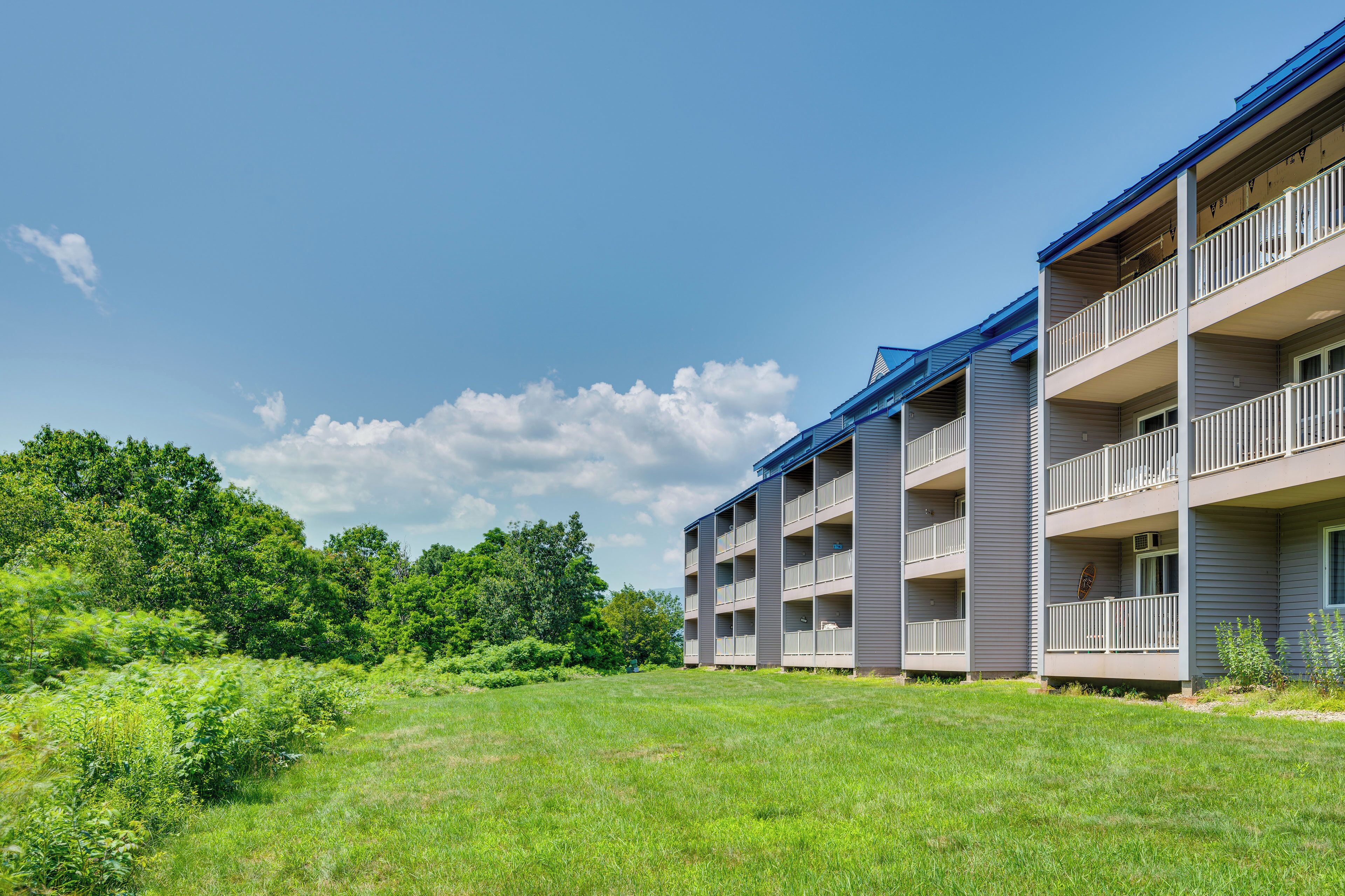 Un immeuble à plusieurs étages doté de balcons, entouré de pelouse verdoyante et d’arbres.