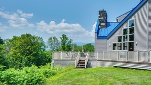 Una casa de dos pisos con techo azul, chimenea de piedra y balcón con escaleras.