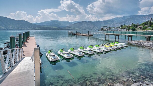 A clear lake with a dock, jet skis, and mountains in the background. - Manson Condo w/ Pool Access - Near Marina and Town (Manson)