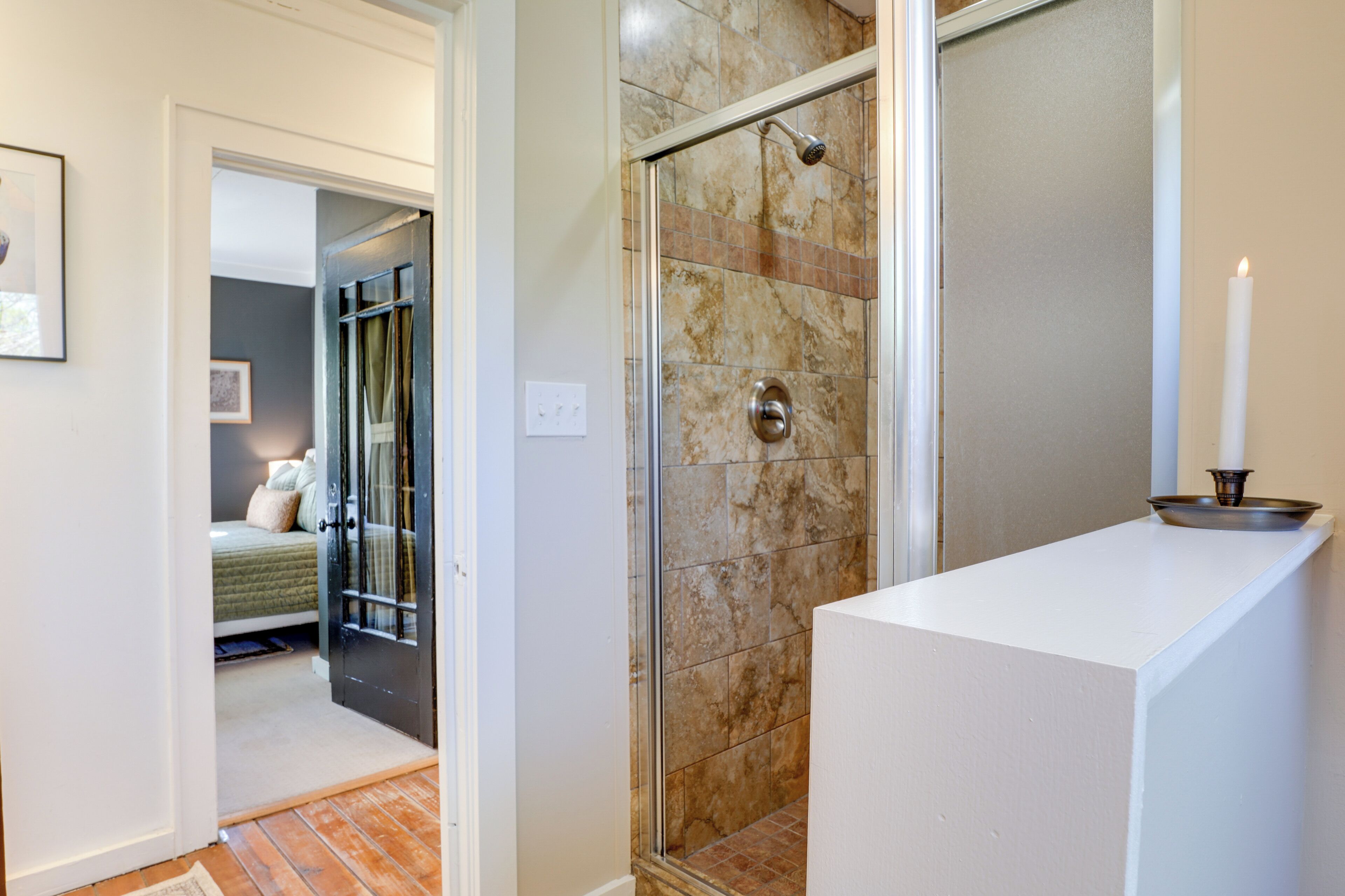 A bathroom with a glass shower enclosure, a white countertop, and a lit candle on a tray.
