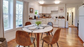 A modern kitchen with white cabinets, a dining table with brown chairs, and a large window with curtains. - Mid-century Modern Fayetteville Home Close to Town (Fayetteville)