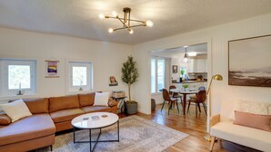 A spacious living room with a large brown sectional sofa, a white round coffee table, and a dining area with a table and chairs.