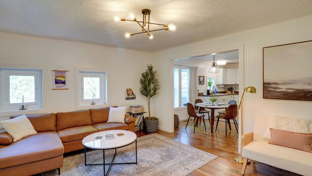 A spacious living room with a large brown sectional sofa, a white round coffee table, and a dining area with a table and chairs. - Mid-century Modern Fayetteville Home Close to Town (Fayetteville)