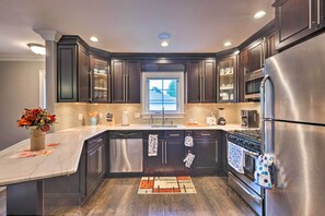 A modern kitchen with dark cabinetry, stainless steel appliances, and a large window providing natural light. - 25 Mi to Nyc: Walkable Long Island Apt w/ Balcony (Glen Cove)