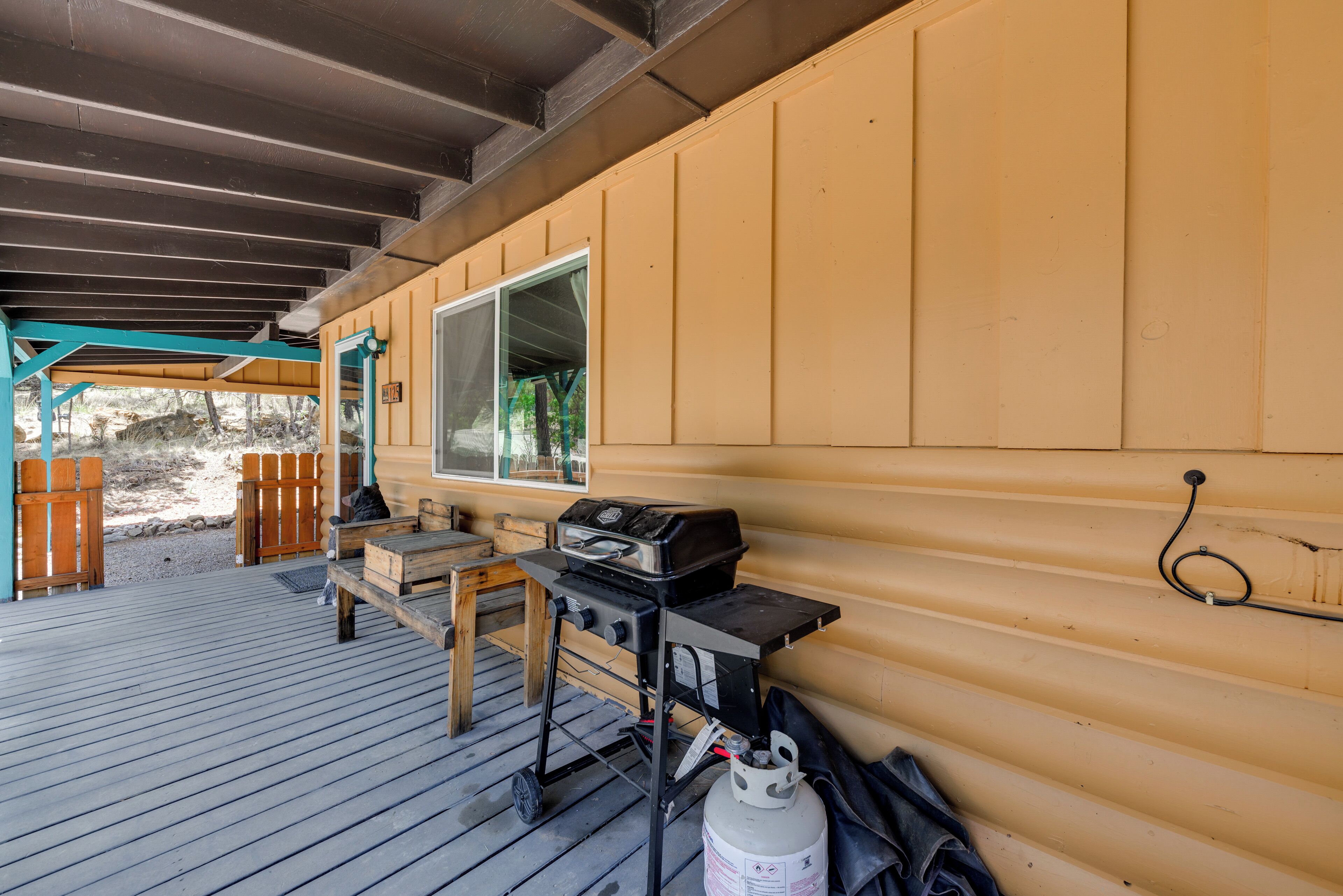 A covered outdoor area with a grill, a gas canister, and a wooden table.
