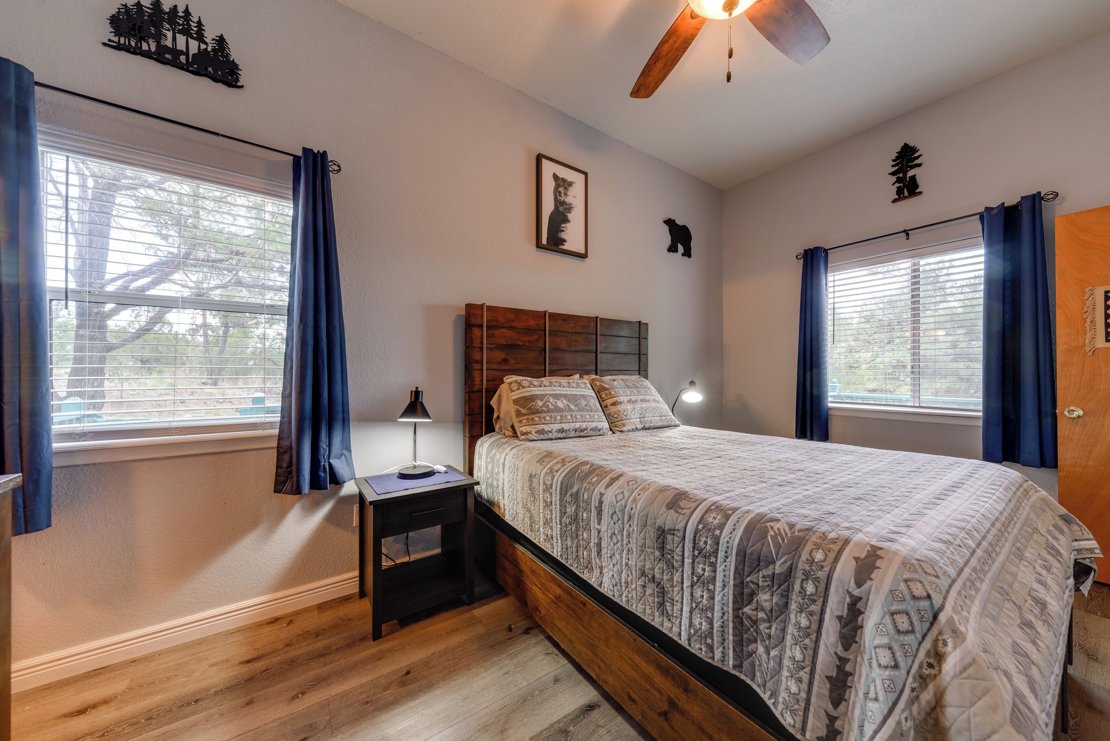 A bedroom with a wooden bed, a nightstand, a ceiling fan, and a window with curtains.