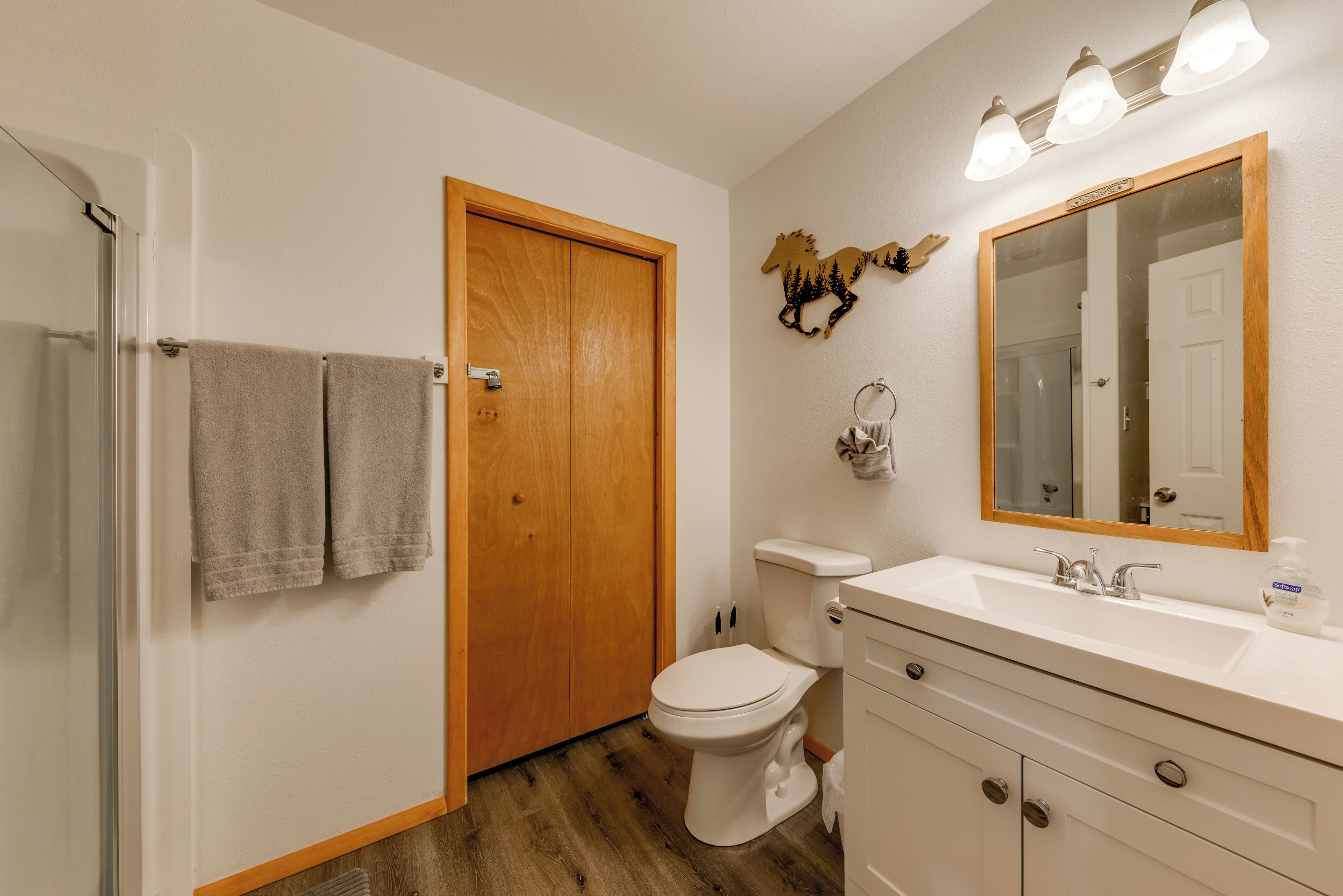 A bathroom with a wooden door, a white toilet, a sink with a mirror, and a towel rack with two towels.