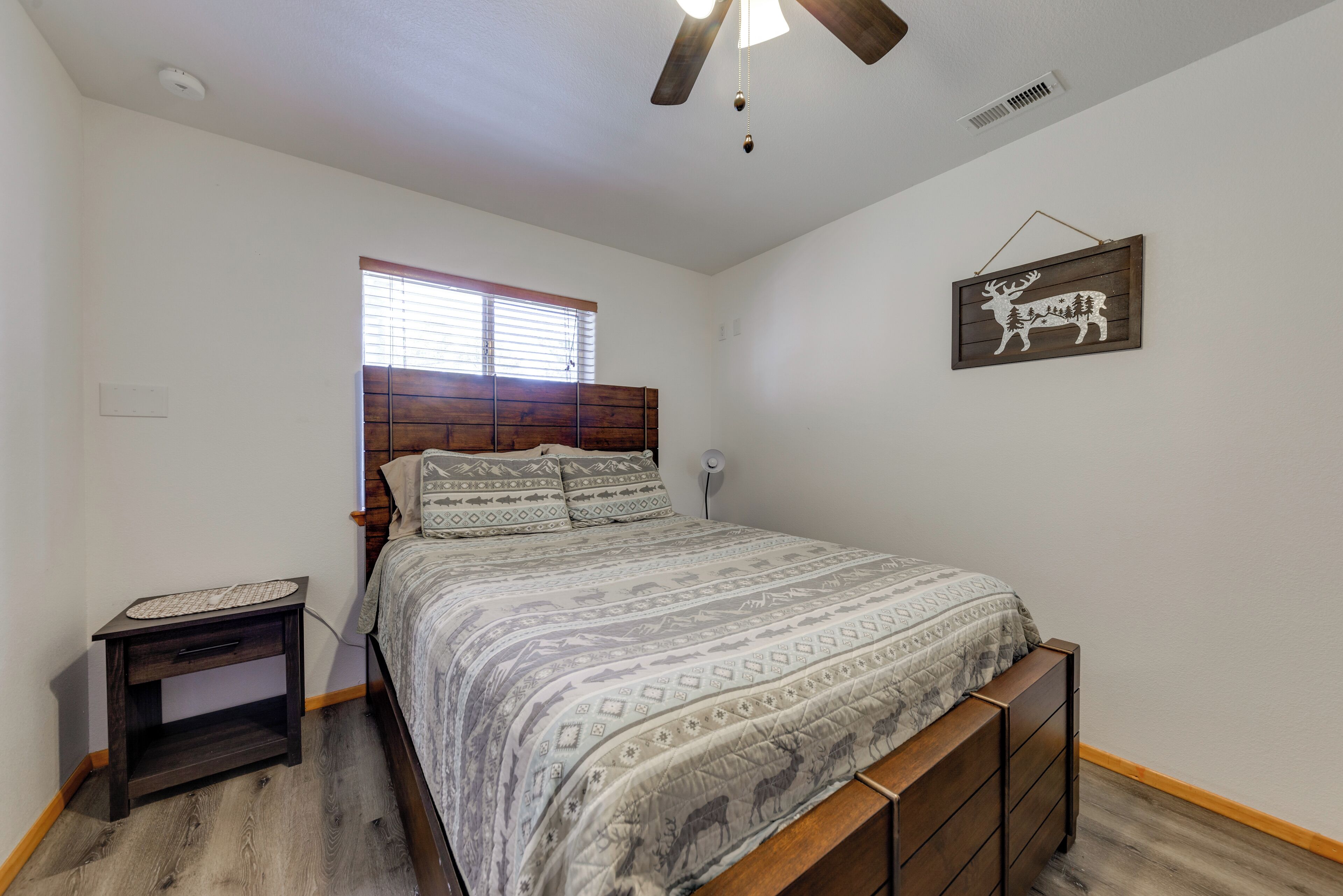 A bedroom with a wooden bed, a nightstand, a window with blinds, and a wall-mounted deer decoration.