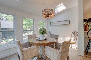 Un coin repas avec une table ronde, des chaises en osier, un lustre et une vue sur l’extérieur.