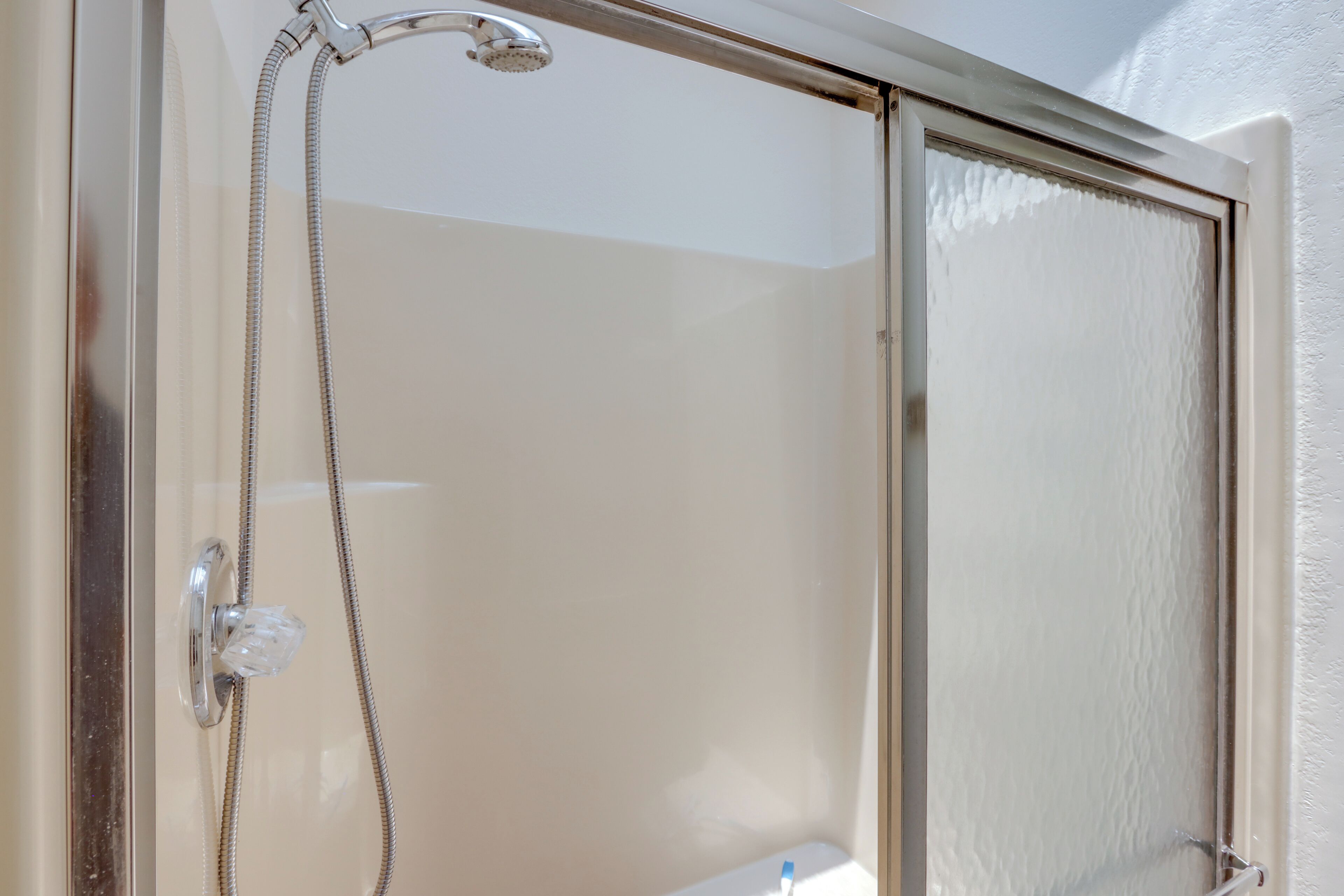 A glass-enclosed shower with a handheld showerhead and a control knob.