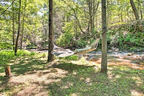 Un hamac installé dans une zone boisée, près d’un ruisseau.