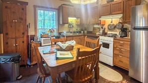 A kitchen with wooden cabinets, a stove, a refrigerator, and a dining table with chairs.