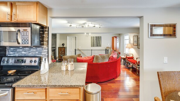 A kitchen with granite countertops, stainless steel appliances, and wooden cabinets. There is a red sofa in the living area with a view of the dining room. - Families w/ Pets! Home 8 Mi to Dtwn Minneapolis (Golden Valley)