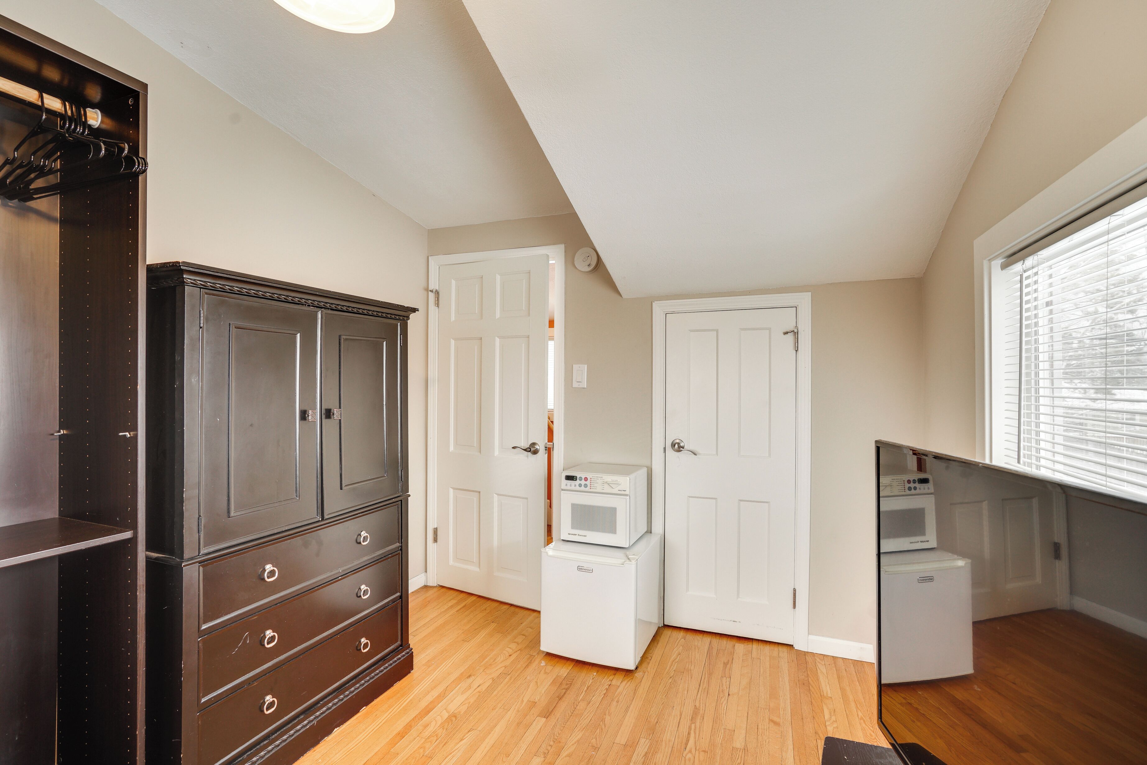 A room with a dark wooden wardrobe, white doors, and built-in appliances including a microwave and a washing machine.
