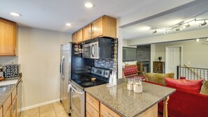 A kitchen with granite countertops, stainless steel appliances, wooden cabinets, and a red sofa in the adjacent living area. - Families w/ Pets! Home 8 Mi to Dtwn Minneapolis (Golden Valley)