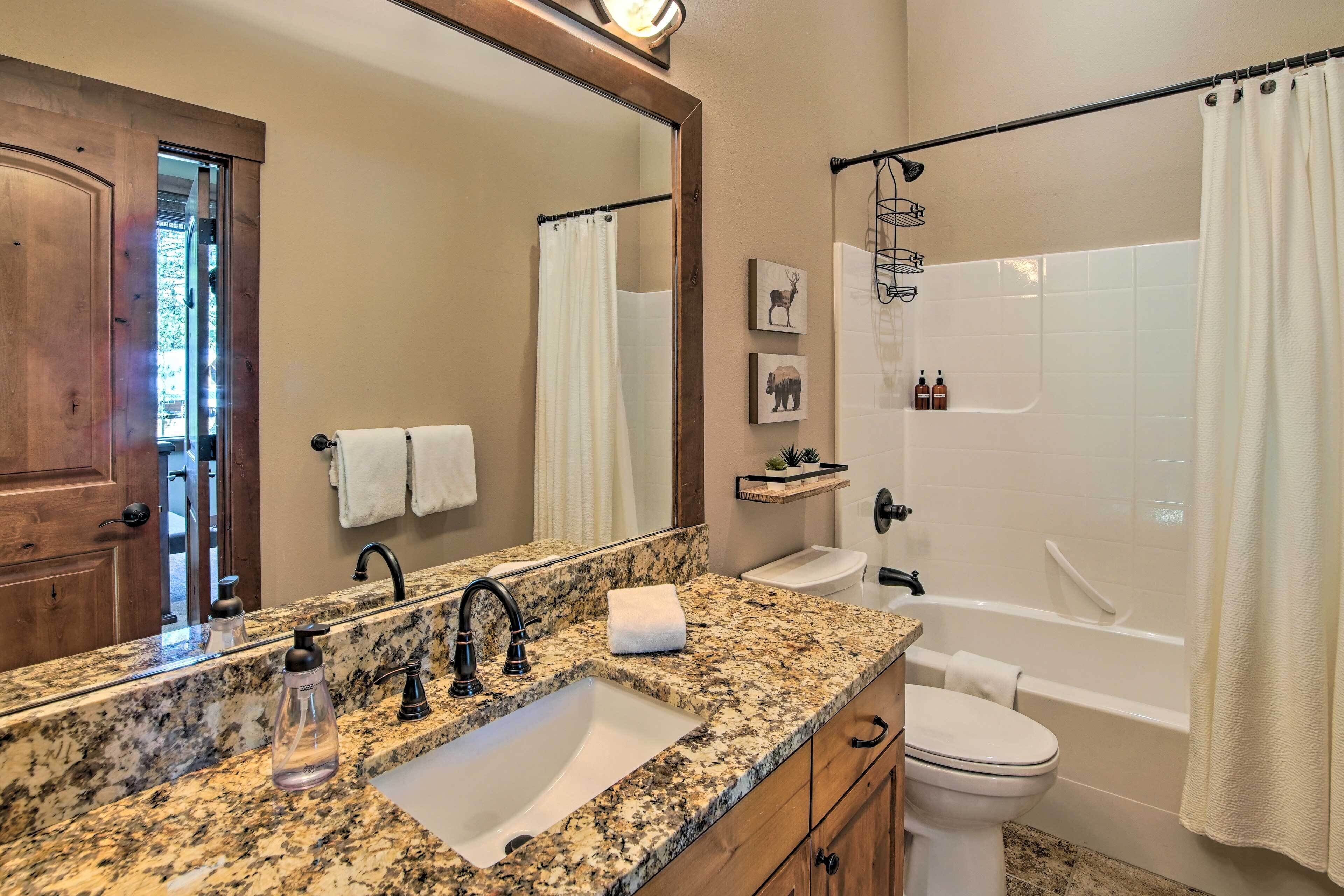 A bathroom with a granite countertop sink, a mirror, a toilet, and a bathtub.