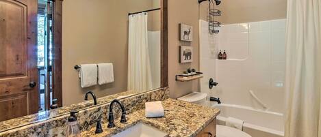 A bathroom with a granite countertop sink, a mirror, a toilet, and a bathtub.