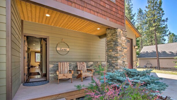A wooden porch with two chairs and a welcome sign, a stone pillar, and a small garden with pink flowers. - Modern-rustic Ronald Getaway: Hot Tub, Grill! (Cle Elum)
