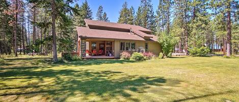 A two-story house with a front porch, surrounded by a well-maintained lawn and tall pine trees.