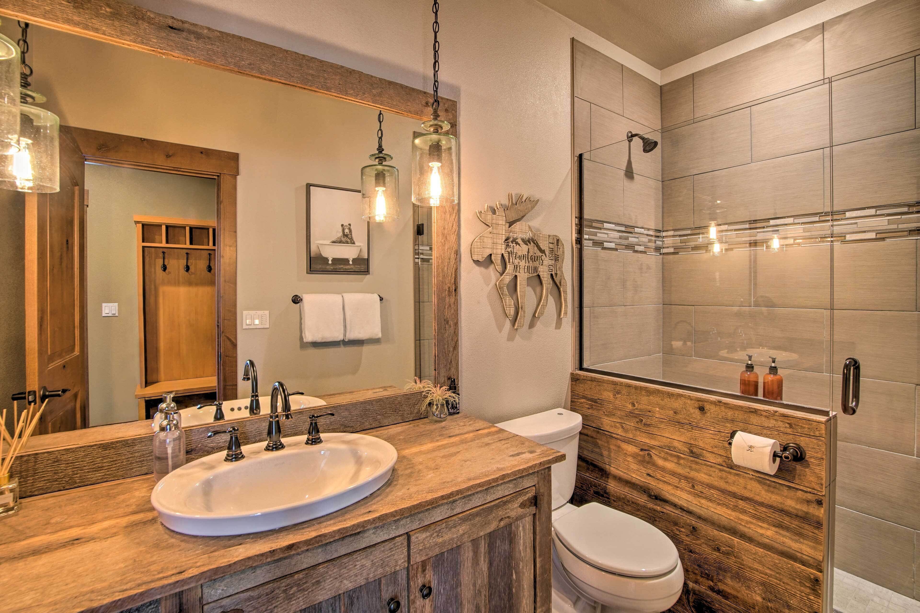 A bathroom with a wooden vanity, a large mirror, a sink, a toilet, and a shower area.