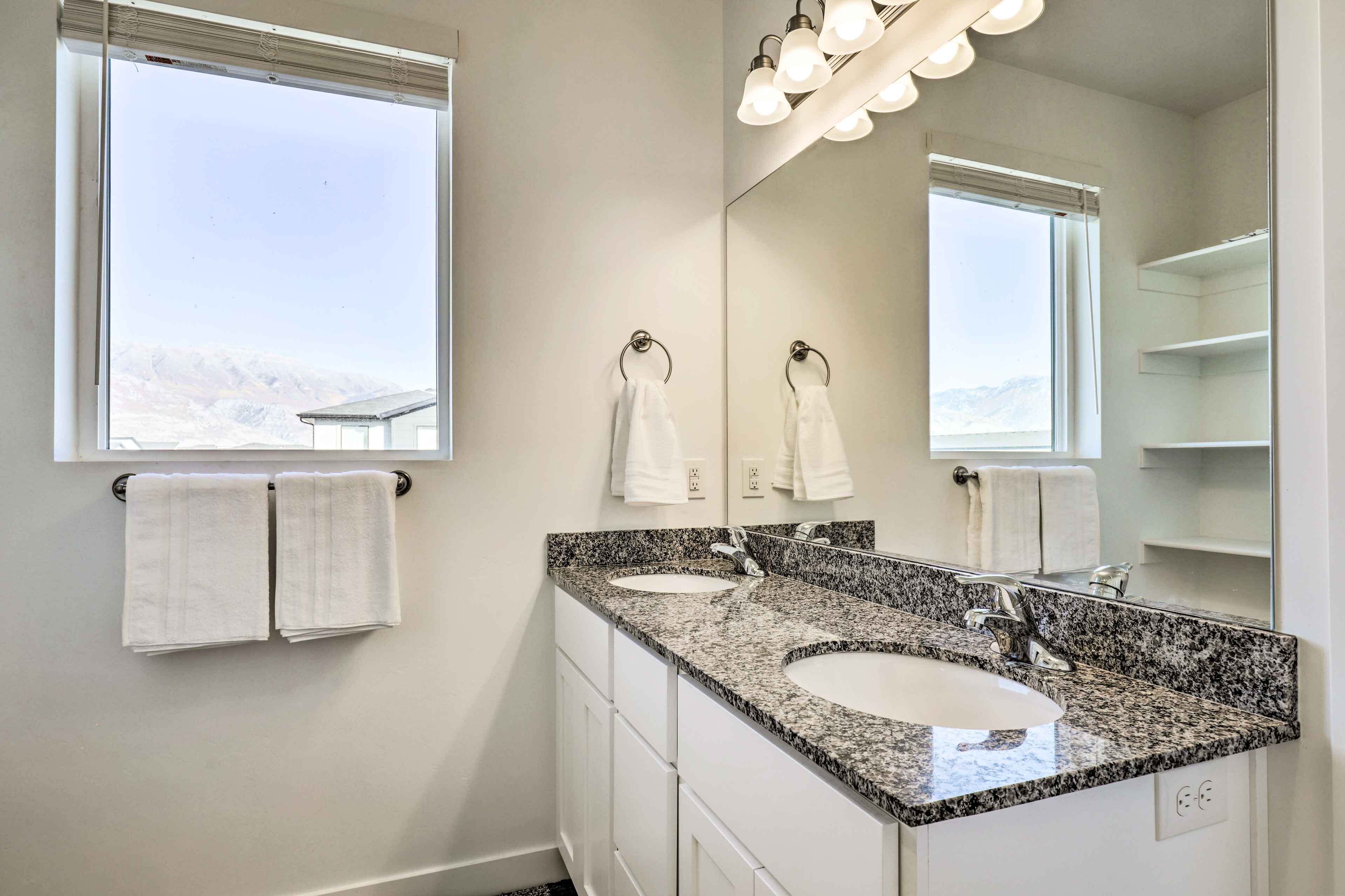 A bathroom with two sinks, a large mirror, and a window with towels hanging on the wall.