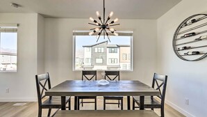 A dining area with a large wooden table, four chairs, a modern chandelier, and a wine rack on the wall. - Modern Townhome - 8 Mi to Thanksgiving Point! (American Fork)