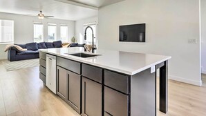 A modern kitchen with a central island, built-in appliances, and a dining area with a sofa and a TV. - Modern Townhome - 8 Mi to Thanksgiving Point! (American Fork)