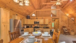 A wooden cabin kitchen with a dining table set for four, a refrigerator, microwave, and a stove. - Hot Tub Soaks! 'moonshine Manor' Near Lake Lure (Lake Lure)