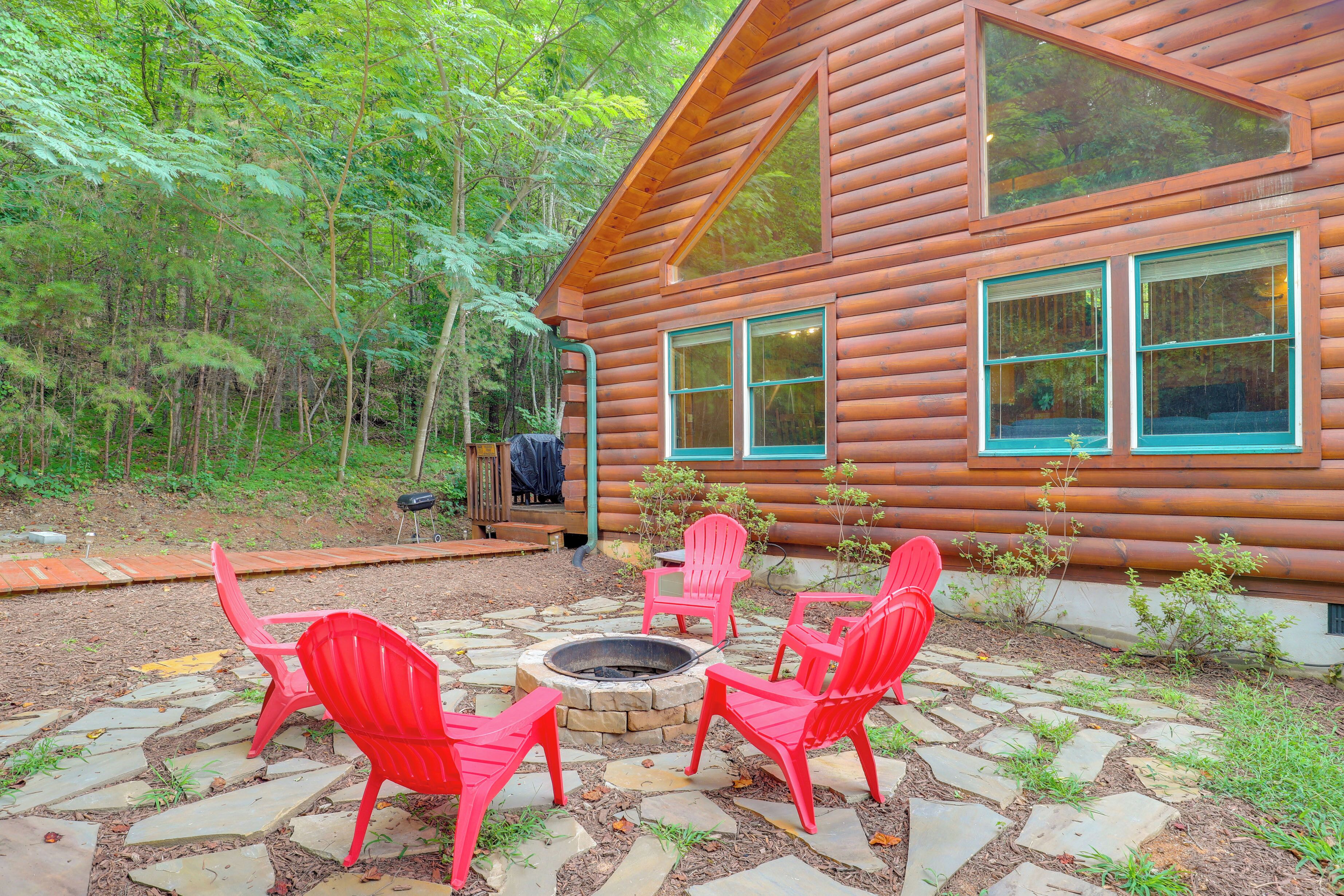 A log cabin with a stone patio, red chairs, and a fire pit.