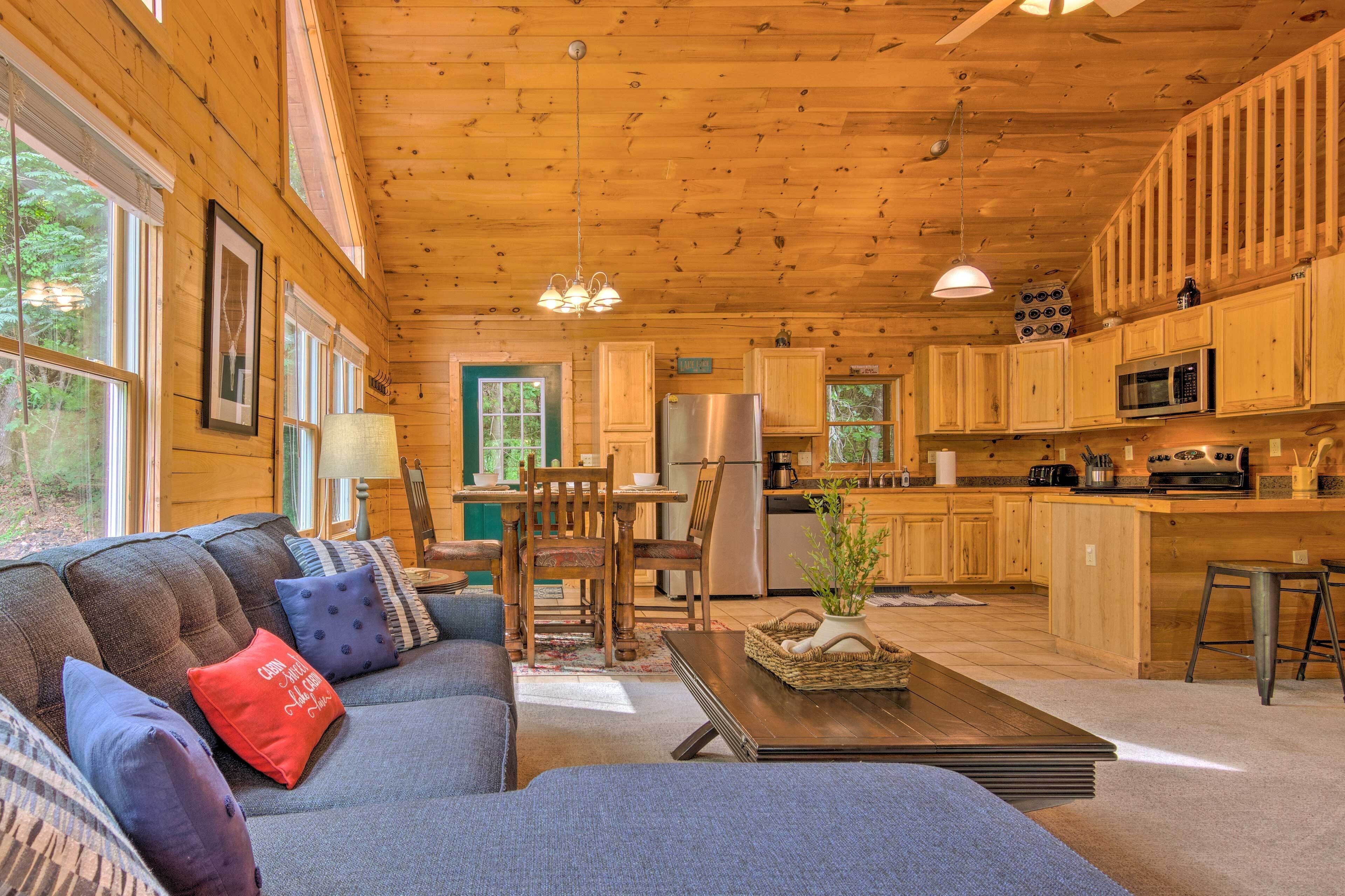 Interior acogedor de una cabaña con un comedor de madera, una cocina con electrodomésticos modernos y una zona de estar confortable con sofá y cojines.