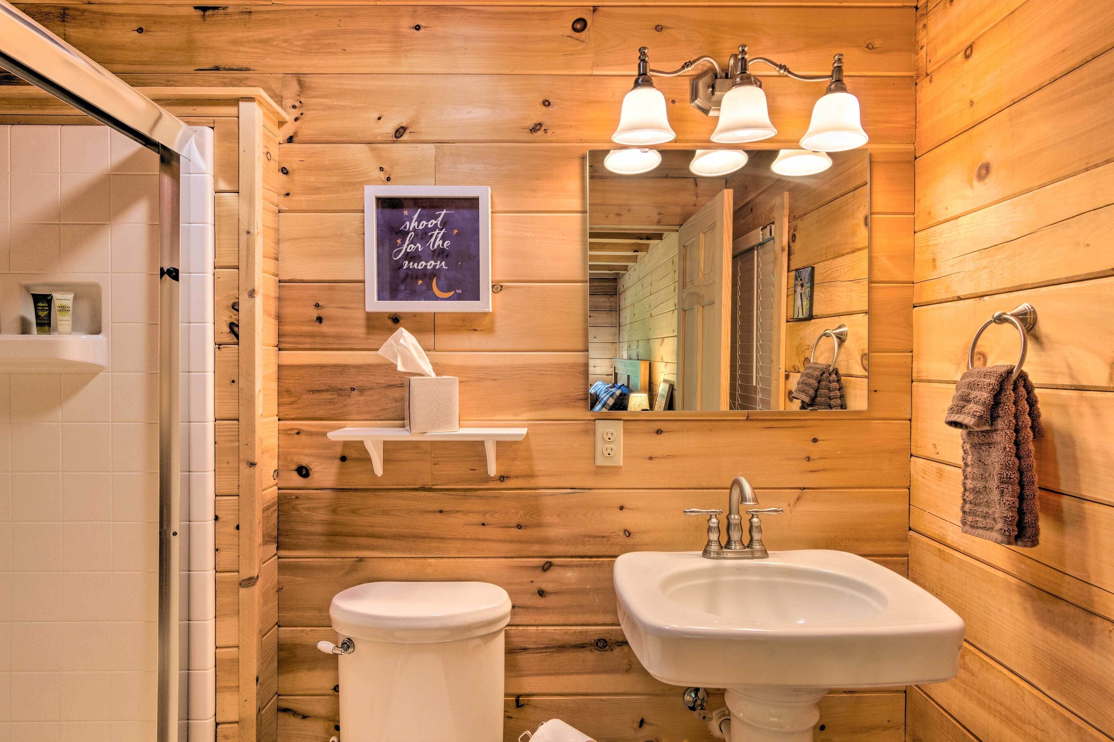 A wooden-paneled bathroom with a toilet, sink, and mirror. There is a towel rack with a towel hanging on it, and a framed sign on the wall.