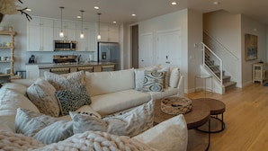 A modern living room with a beige sofa, patterned cushions, a round coffee table, and a kitchen in the background. - Hot Tub: Heber City Home 15 Mi to Park City! (Heber City)