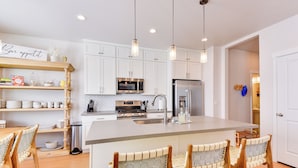 A modern kitchen with white cabinets, a stainless steel refrigerator, a microwave, and a large island with bar stools. - Hot Tub: Heber City Home 15 Mi to Park City! (Heber City)