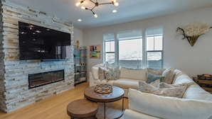 A modern living room with a stone fireplace, a white sofa, and a round coffee table. - Hot Tub: Heber City Home 15 Mi to Park City! (Heber City)