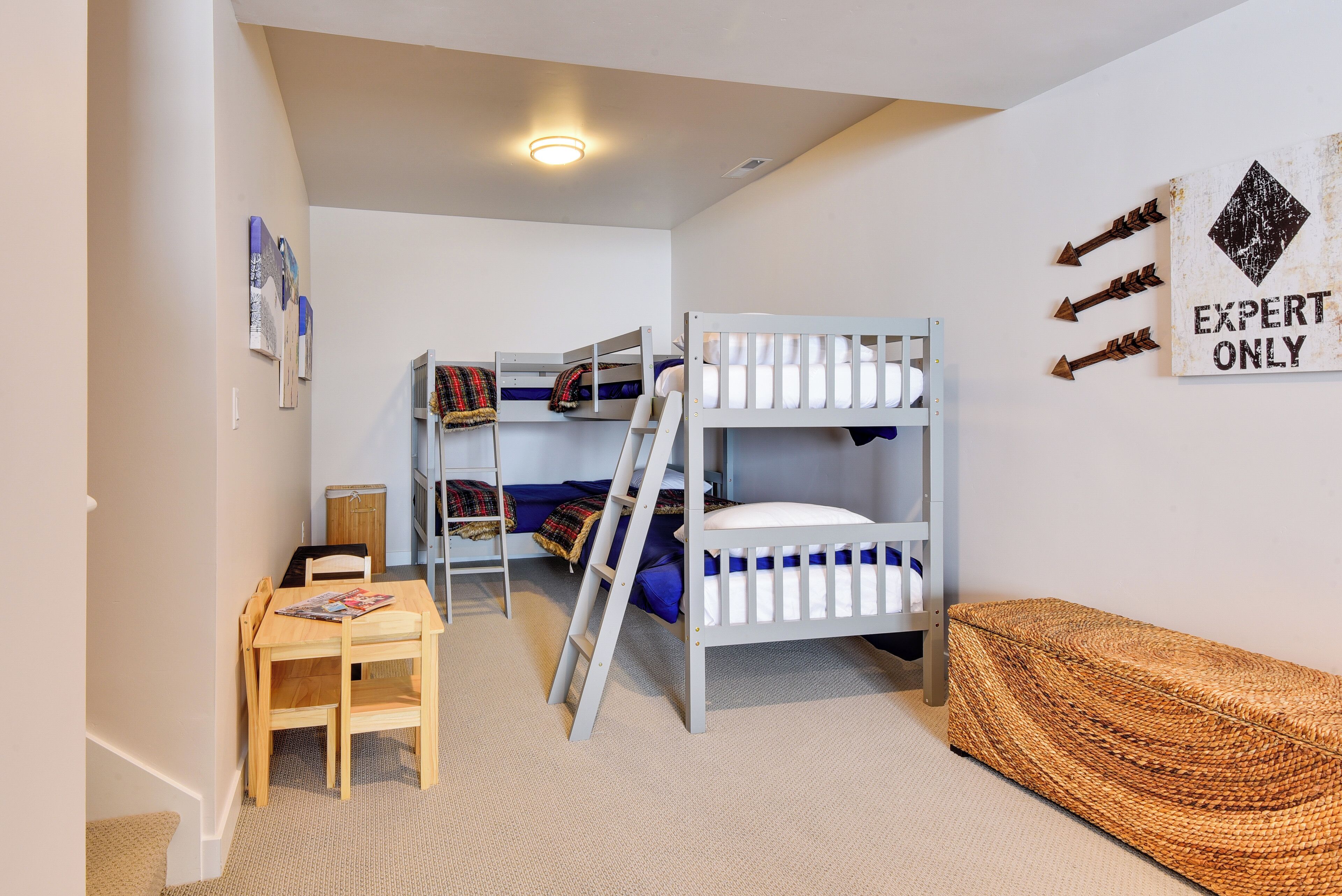 A bunk bed room with a desk and chair, a ladder, and a woven bench.