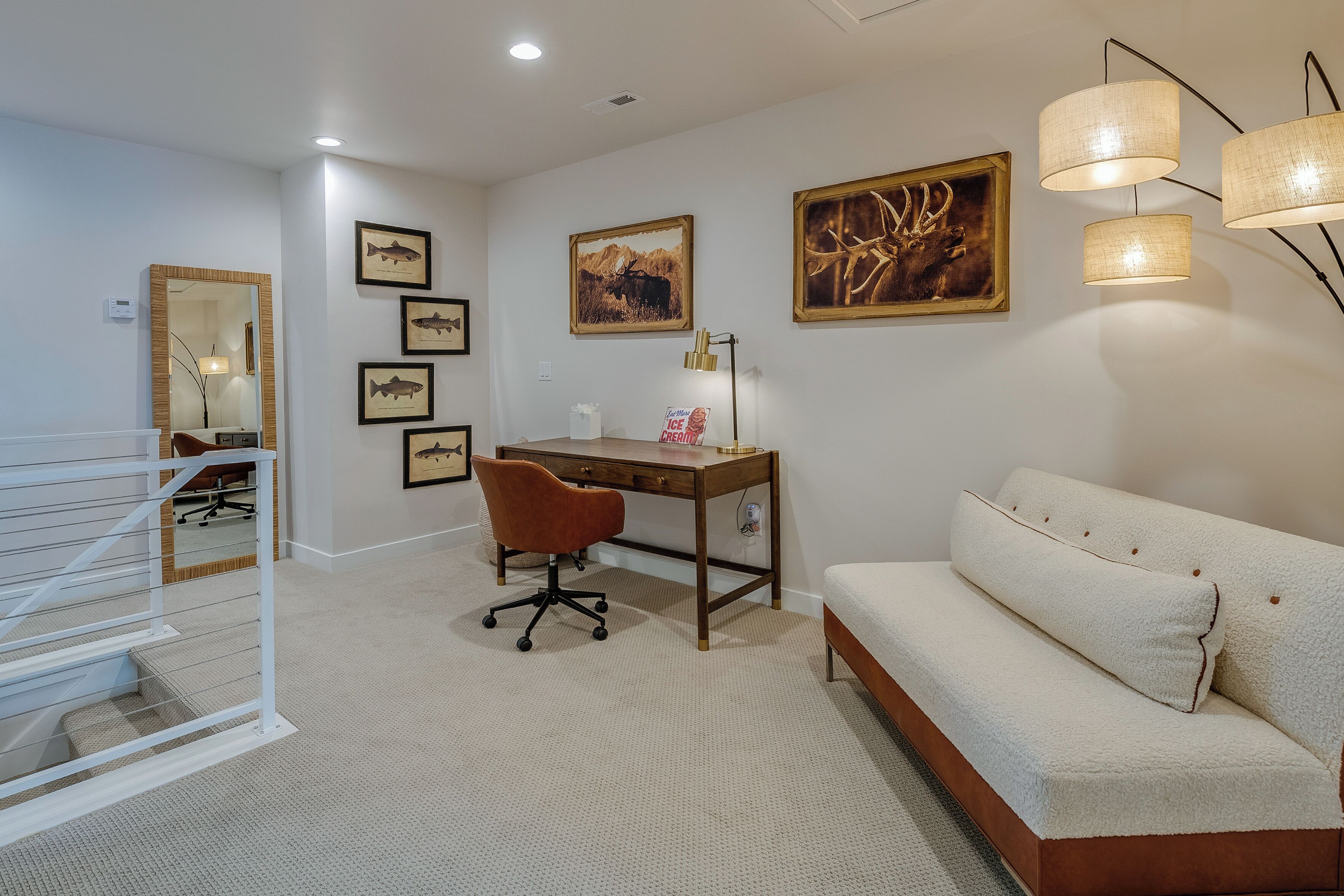 Une chambre moderne comprenant un bureau, un canapé, une chaise et des œuvres d’art accrochées au mur.