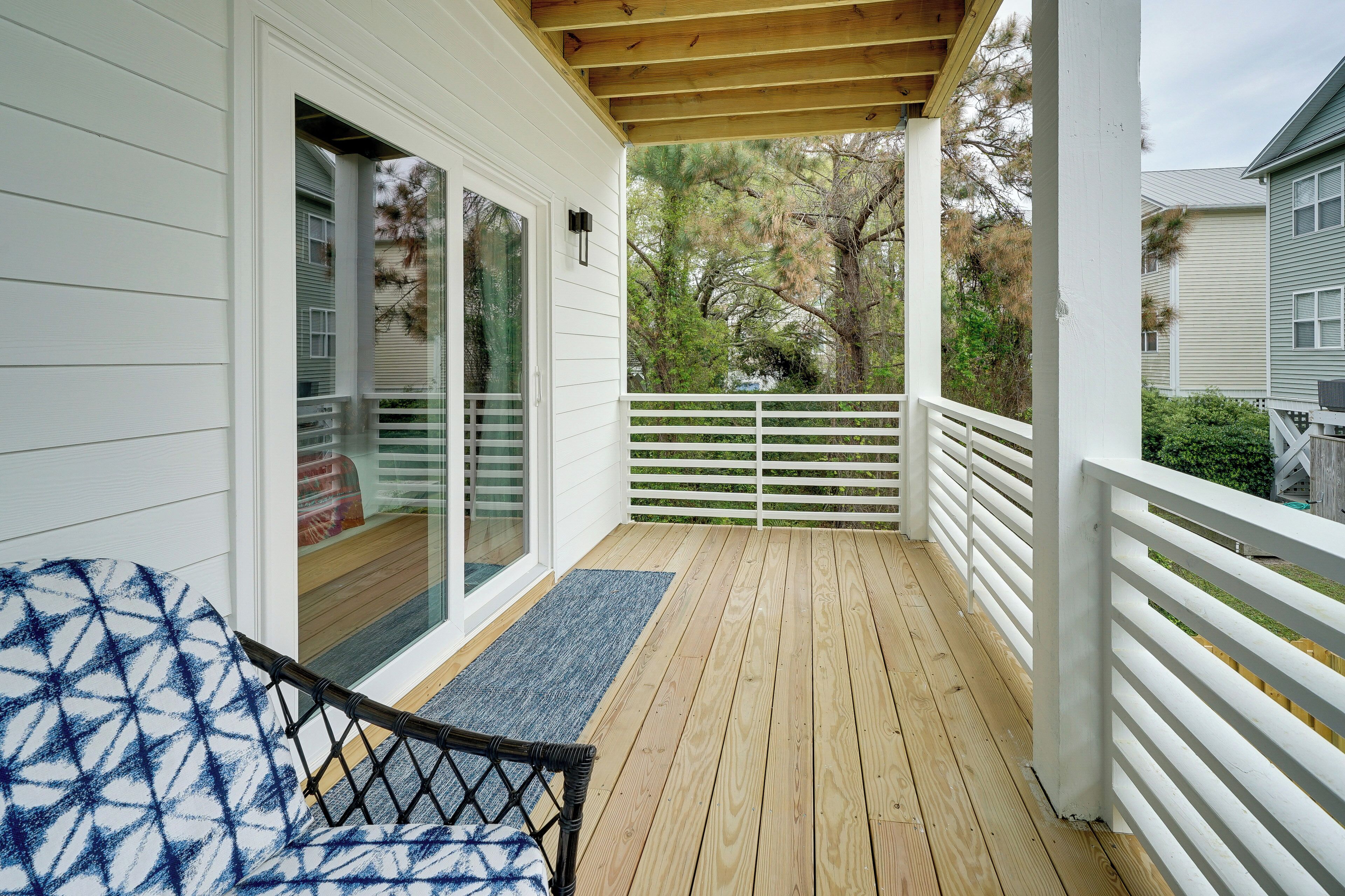 A covered porch with a wooden floor, white railings, and a glass door leading to a room.