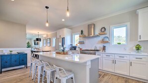 A modern kitchen with white cabinets, a large island with bar stools, and pendant lighting. - Modern Home w/ Rooftop Deck, Walk to Beach! (Carolina Beach)