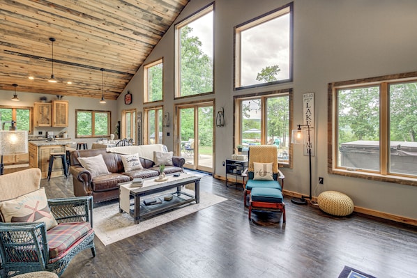 A spacious living room with a high ceiling, large windows, and a view of the outdoors. - Modern Lakeside Chalet on Crow Wing Chain w/ Dock! (Nevis)