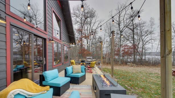 An outdoor patio with seating, a fire feature, and string lights. - Modern Lakeside Chalet on Crow Wing Chain w/ Dock! (Nevis)