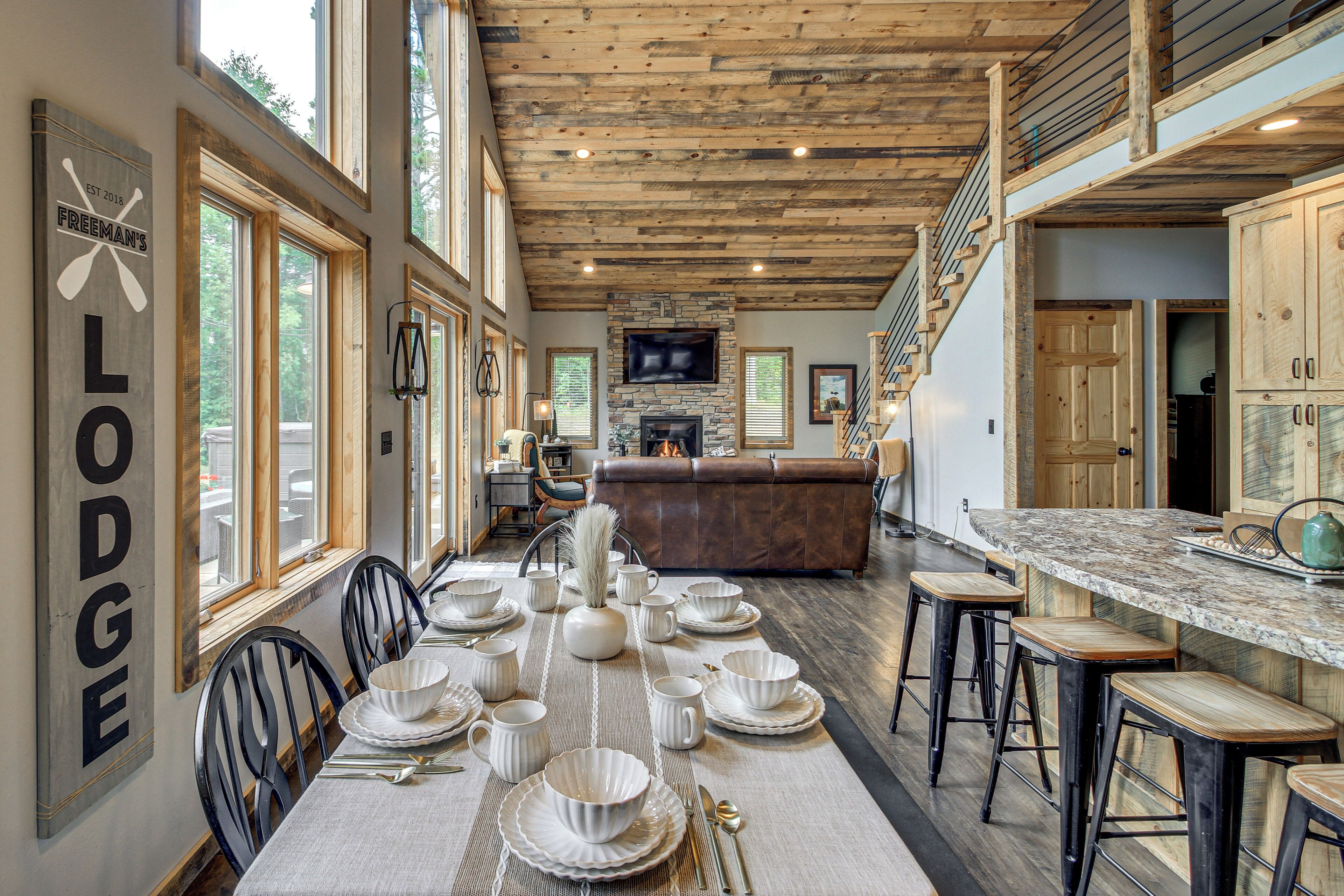 Interior espacioso de una cabaña con comedor listo para una comida, chimenea de piedra y cocina con una isla grande.