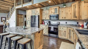 A kitchen with wooden cabinets, stainless steel appliances, a granite countertop, and a bar area with stools. - Modern Lakeside Chalet on Crow Wing Chain w/ Dock! (Nevis)