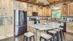 A kitchen with wooden cabinets, stainless steel appliances, a granite countertop, and bar stools. - Modern Lakeside Chalet on Crow Wing Chain w/ Dock! (Nevis)