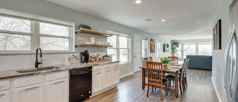Una cocina amplia con armarios blancos, lavavajillas y una zona de comedor con sillas y mesa de madera.